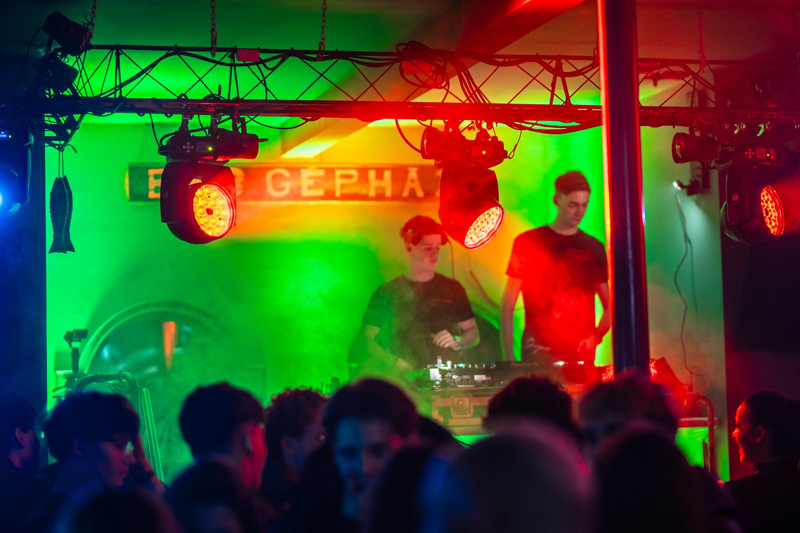 Silhouetted crowd on a dark underground dancefloor, cut by a single beam of light.