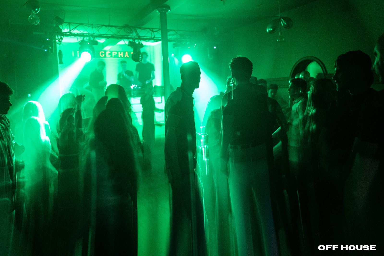 Crowd silhouettes at an intimate underground OFF HOUSE event, lit by warm red light.